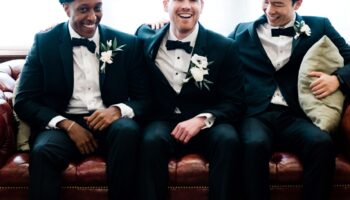 Small Prep Suite Groom and Groomsmen Sitting on Sofa Laughing Getting Ready Garey House Natural Lighting